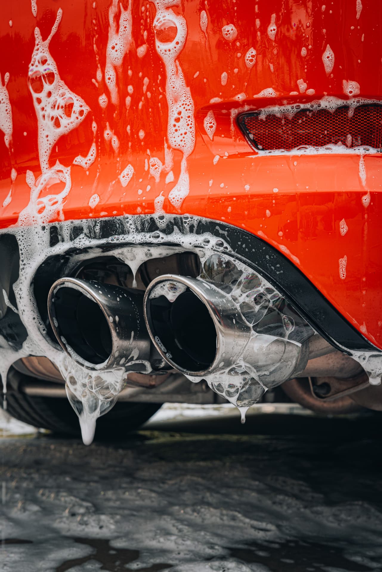 Foam washing the rear bumper and exhausts of a red car